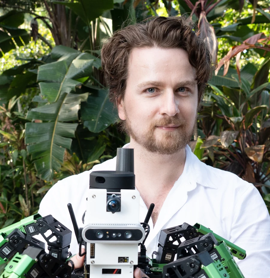 Dr Adam D Hines holding a hexapod robot in a garden